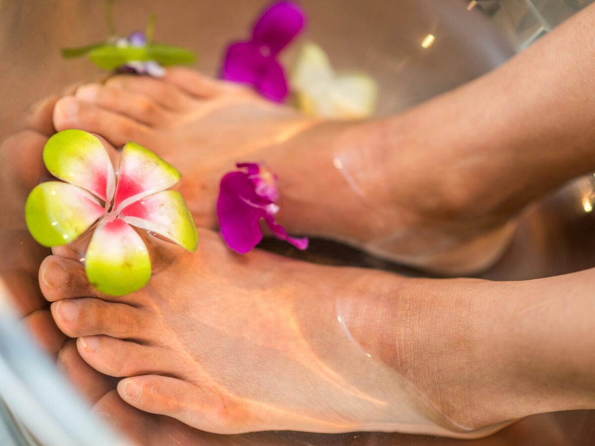 A therapist working on a client's foot over a flower-filled foot bath